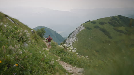 a young hiker waliking on a narrow path up a hill with hiking poles an carrying a grey backpack in background are visible some other mountains but are covered in low cloud cover