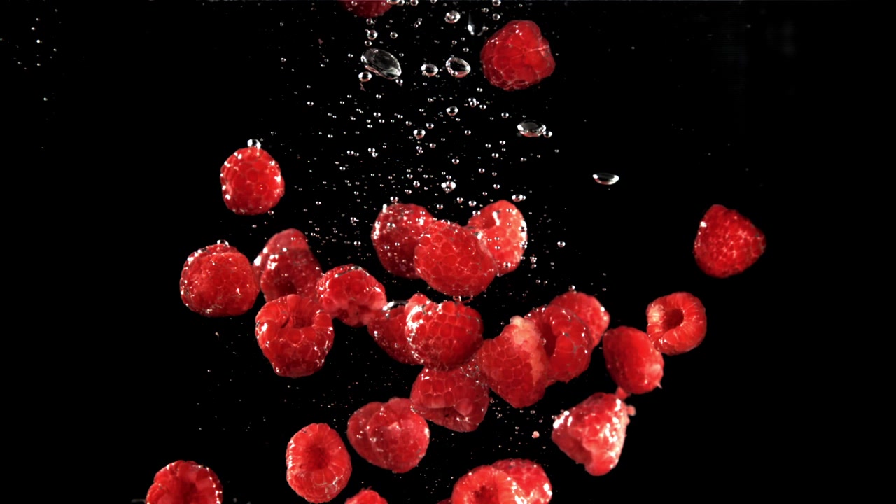 Fresh Red Raspberries Floating in Water Against Black Background