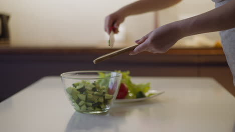 woman puts cucumber slices into glass bowl on table