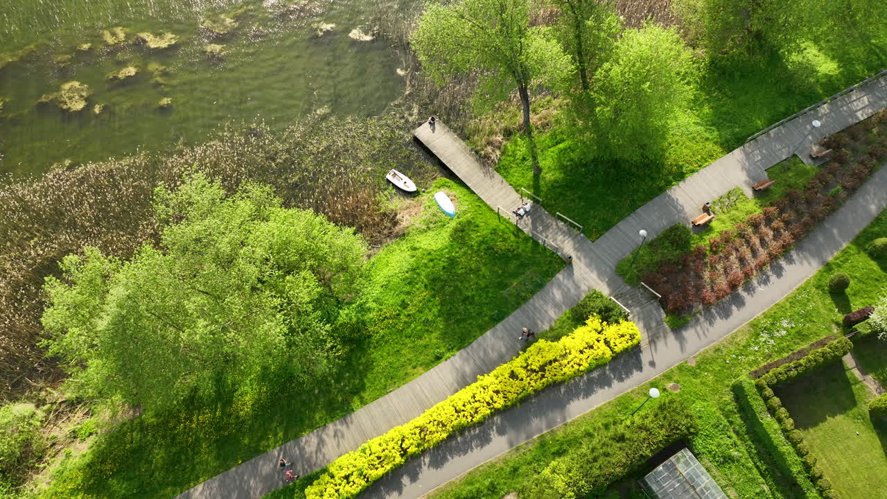 сверху вниз воздушный снимок, изображающий богатые текстуры и цвета реки с лодками, пришвартованными вдоль небольшого причала, окруженным густой зеленой листвой и хорошо ухоженной дорожкой