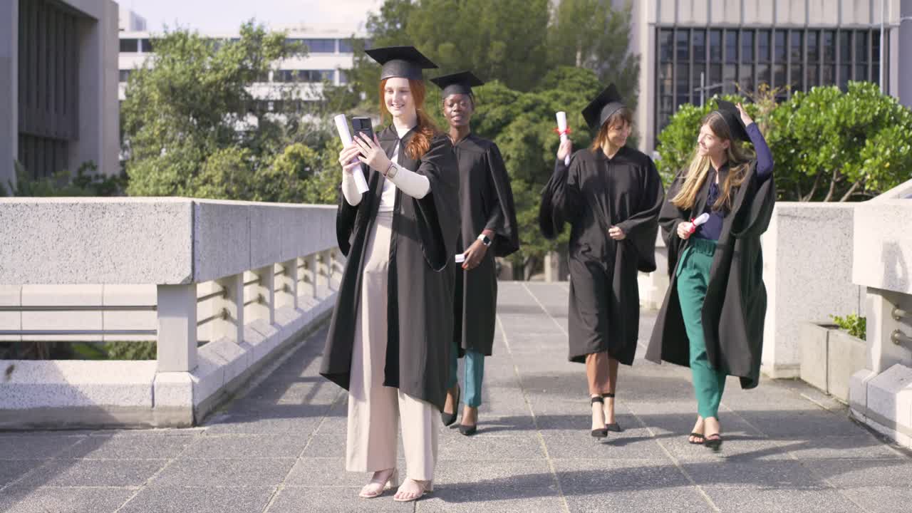 Laureate che festeggiano scattando un selfie con telefono e diplomi mentre gli amici si avvicinano nel campus