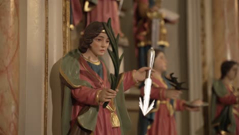 colorful wooden saint statue holding palm frond and arrow in an ornate church interior