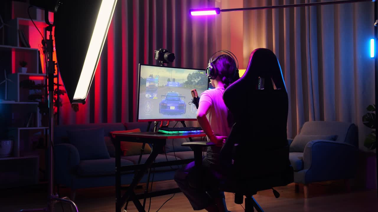개인 컴퓨터에서 네트워크를 통해 자동차 레이싱 게임을하는 동안 허리 통증이있는 아시아 소녀 스트리머의 뒷면. 라이브 스트리밍 비디오 게임, rgb led 스트립 라이트에 의해 조명 된 책상