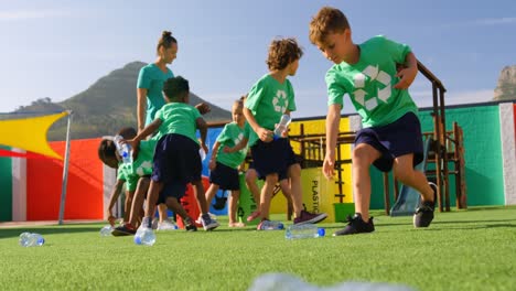 Front-view-of-Caucasian-female-teacher-teaching-schoolkids-about-bottle-recycle-in-the-school-playgr