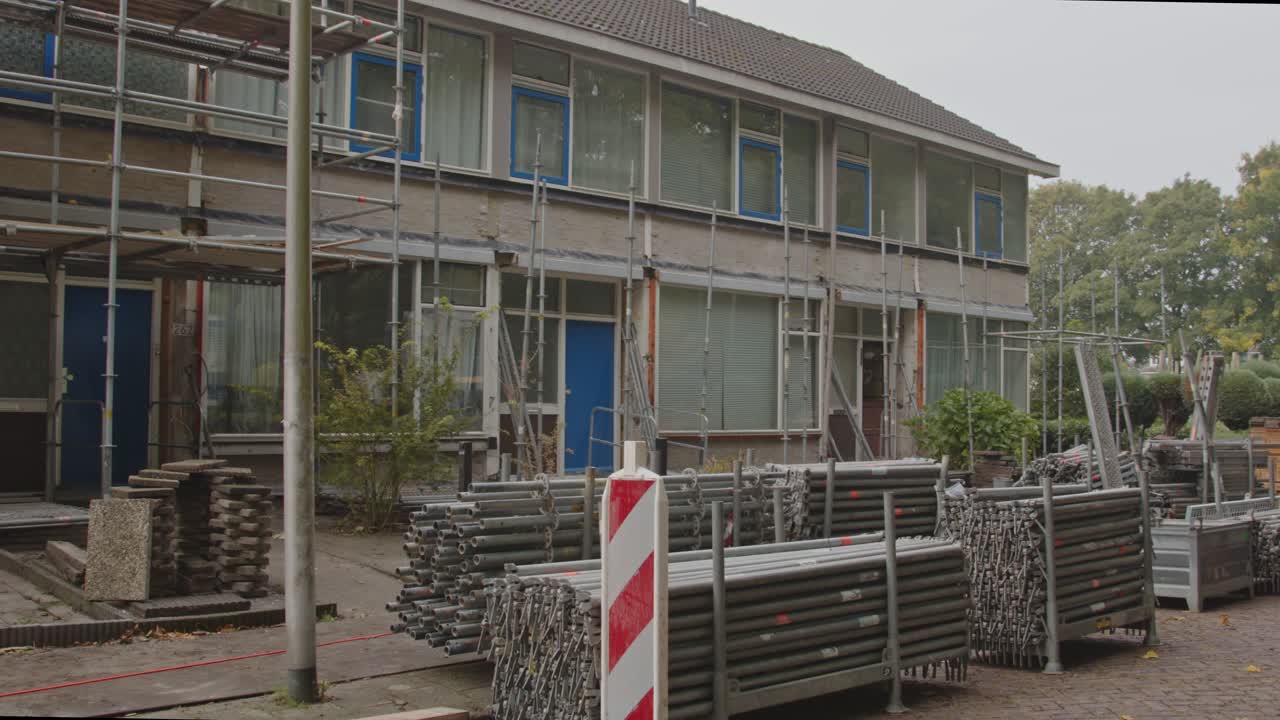 Wide pan of construction materials piled up on the streets in front of a row of houses under renovation