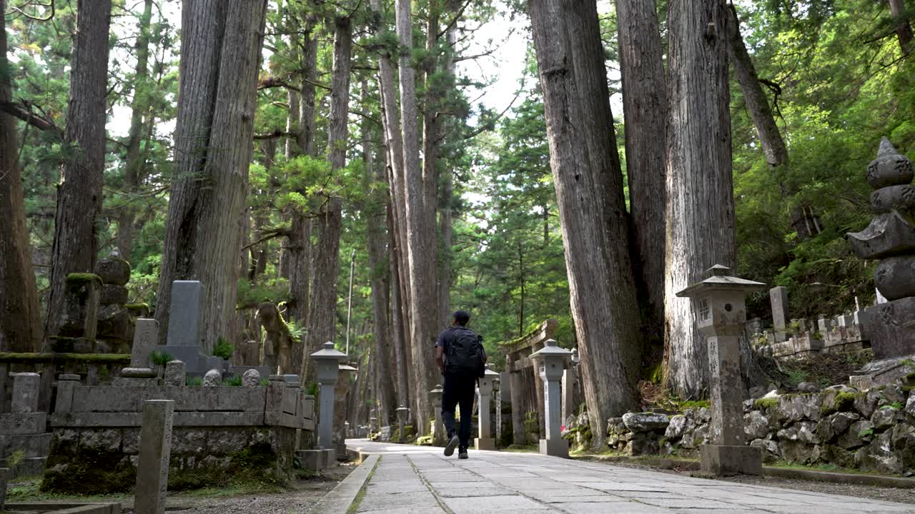 un mochilero solo caminando por el cementerio del bosque de okunoin en wakayama con árboles de cedro en el fondo