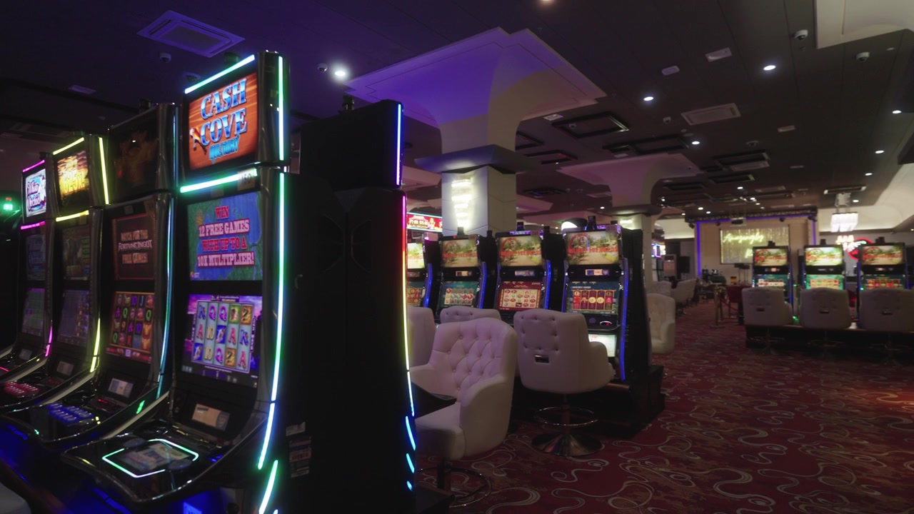 Filmato di un casinò che mostra l'interno, con enfasi su macchine da gioco elettroniche, sedie eleganti e la disposizione principale della sala da gioco del casinò