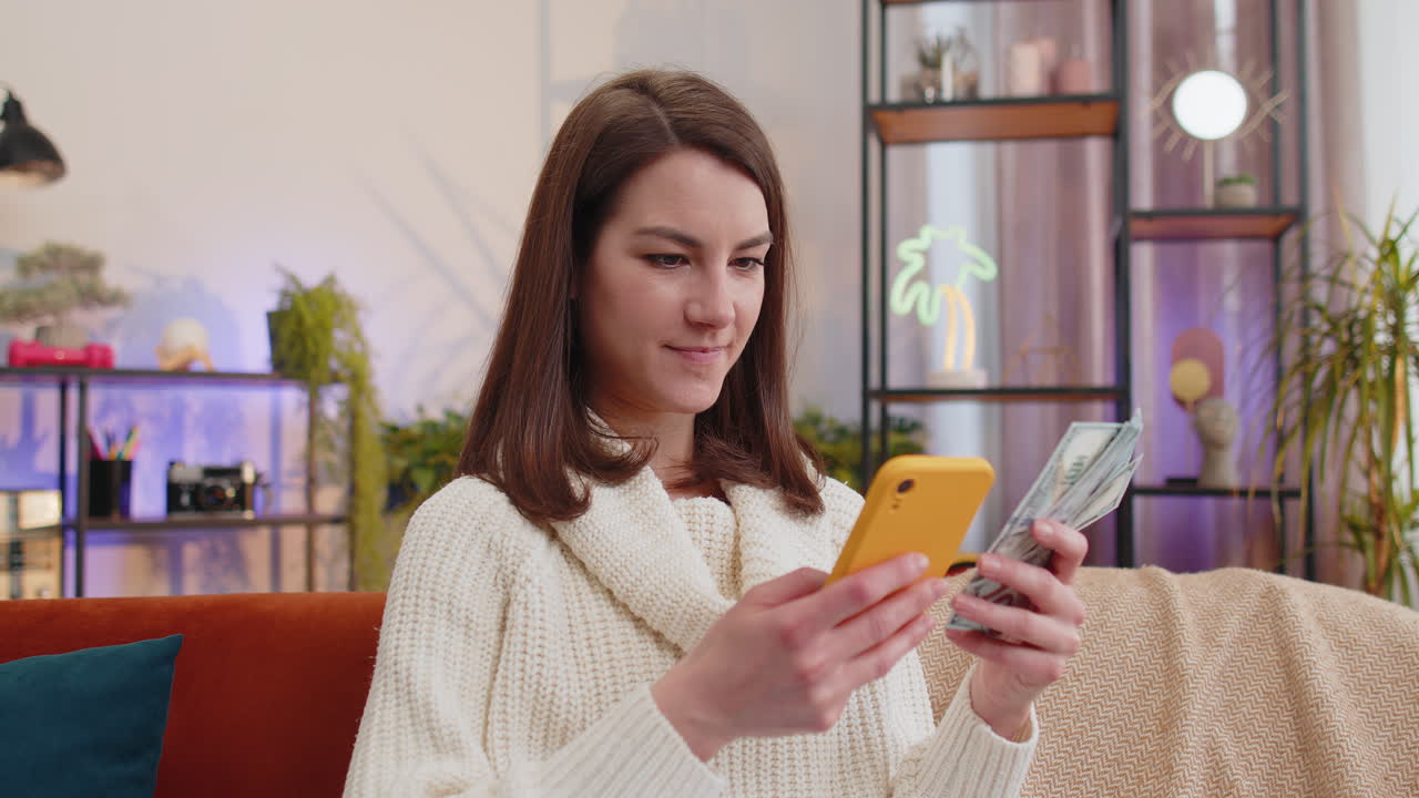 mujer joven sonriente feliz contando dinero en efectivo uso de teléfono inteligente ingresos ahorra lotería ganar presupuesto en casa
