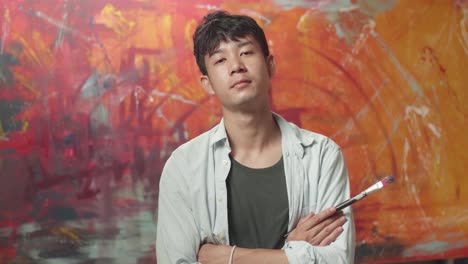 asian male artist painting and looking at abstract painting