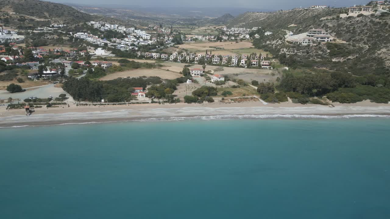fotografía aérea de la playa de pissouri en chipre con aguas azules serenas y un fondo de ciudad costera, a la luz del día