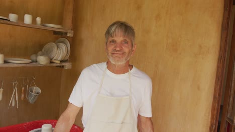 portrait of smiling senior caucasian man wearing apron in pottery workshop