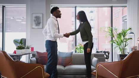 businesswoman shaking hands with male interview candidate in seating area of modern office