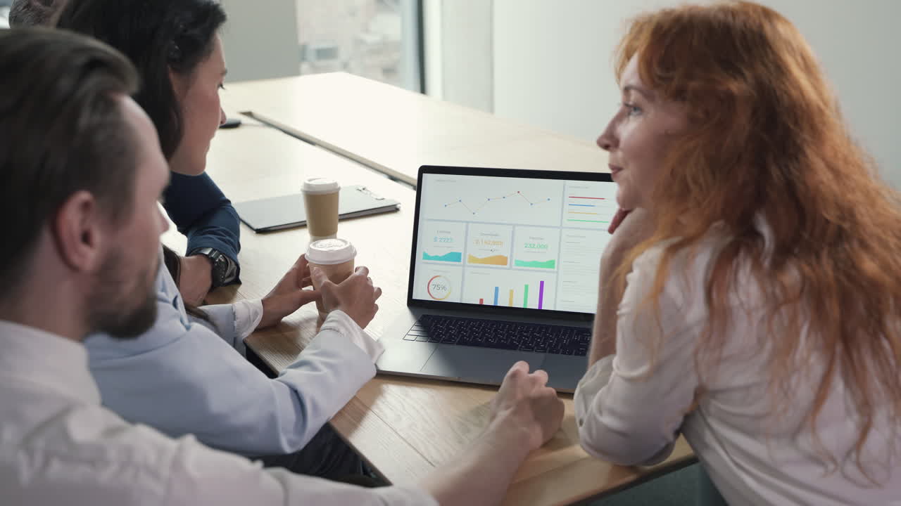 A young working team composed of two women and two men consulting financial results at the laptop in a work meeting