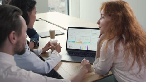 un joven equipo de trabajo compuesto por dos mujeres y dos hombres consultando resultados financieros en la computadora portátil en una reunión de trabajo