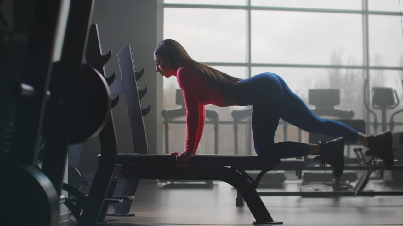 The girl in the blue leggins and short pink top is doing a circular workout in the gym. She pumps the muscles of the buttocks and back of the thigh.