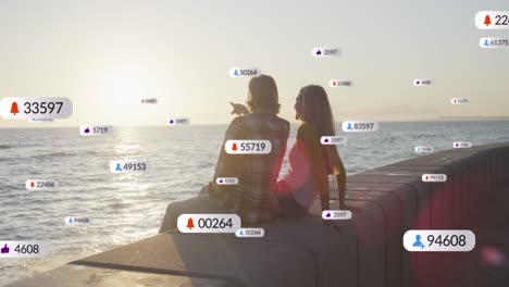 múltiples iconos digitales con números crecientes sobre una pareja caucásica sentada juntos cerca del mar