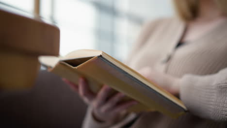 close-up of young lady holding book while reading attentively in cozy, relaxed environment, her fingers gently flip through the pages as she immerses herself in reading