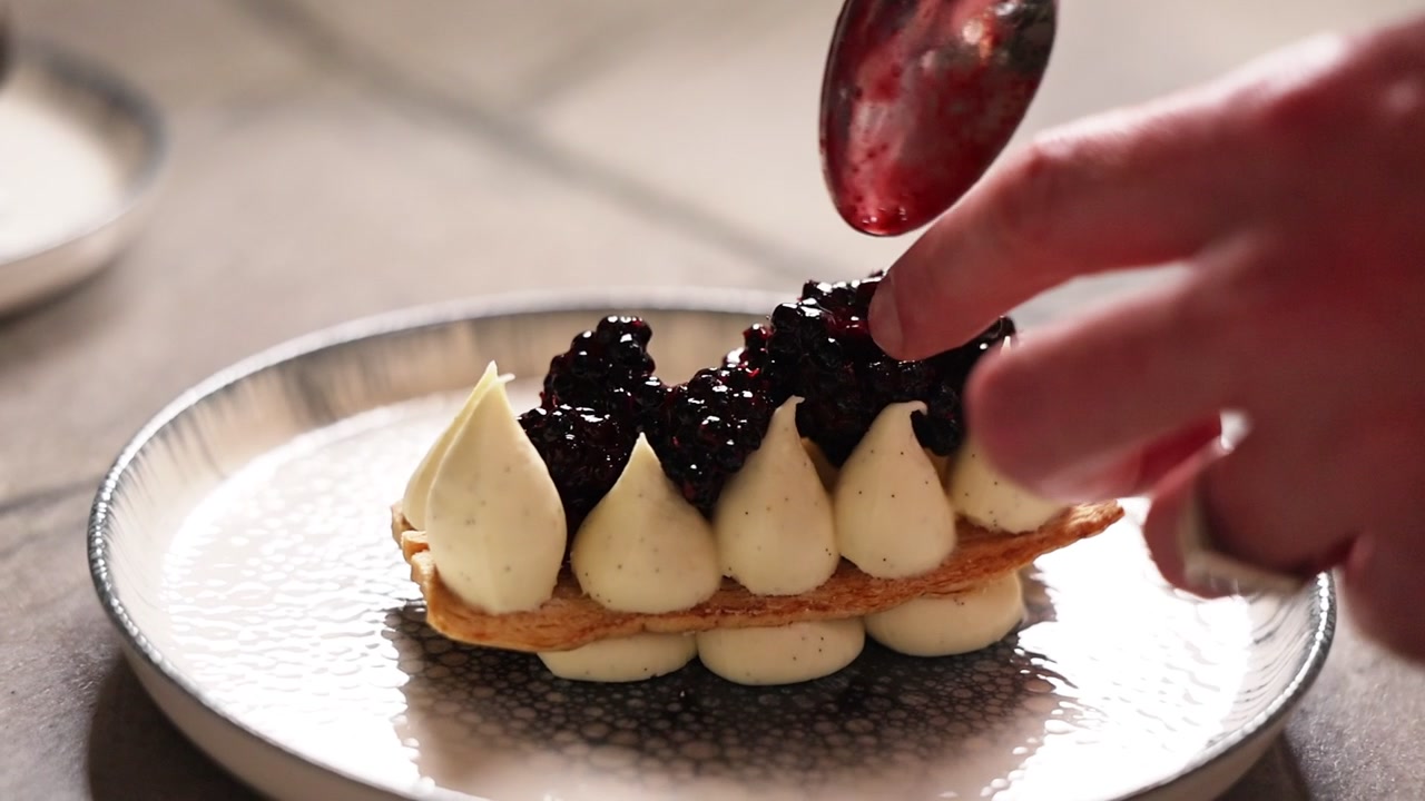 Konditor pynter en gourmetdessert med bjørnebærkrem