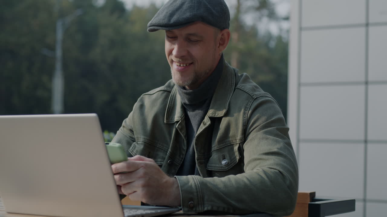 Man Working Outdoors at a Cafe with Laptop and Phone
