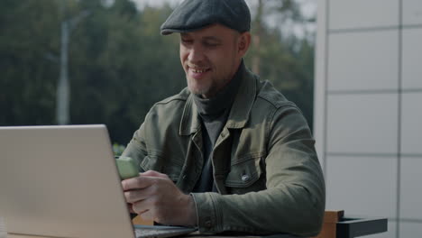 man working outdoors at a cafe with laptop and phone