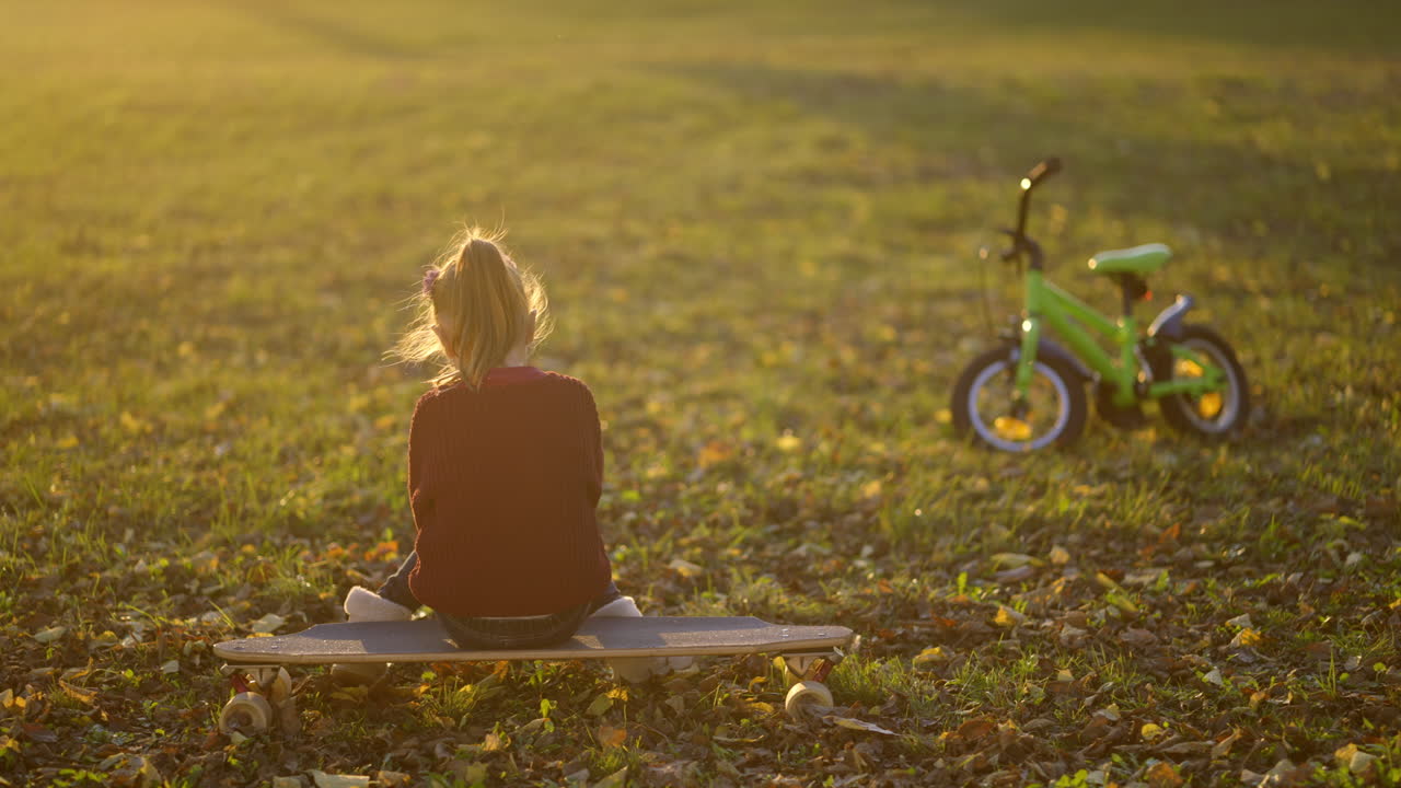 Girl sitting on a skateboard with a bike in a park