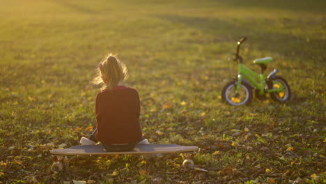 girl sitting on a skateboard with a bike in a park