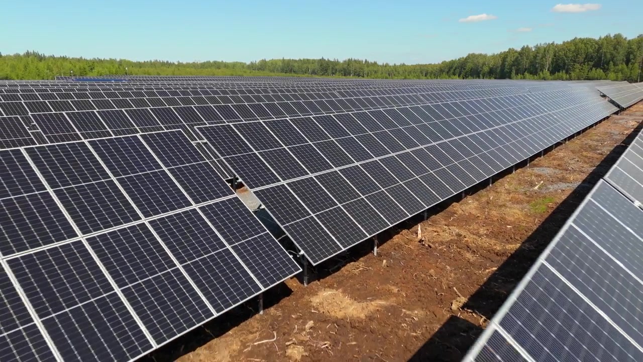 Ripresa aerea veloce con carrello all'indietro a bassa quota sopra i pannelli bifacciali di un parco solare, che mostra la produzione di energia rinnovabile nella foresta.