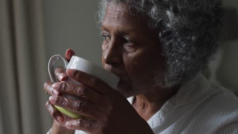 close up of senior african american woman drinking coffee while sitting on the bed at home