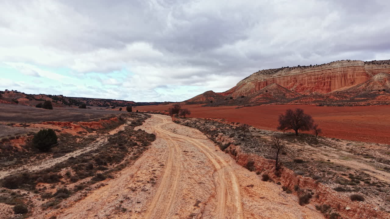 Paesaggio di un canyon con sentiero tortuoso e terreno arido, sotto un cielo nuvoloso, vicino a una zona montana, verso mezzogiorno.