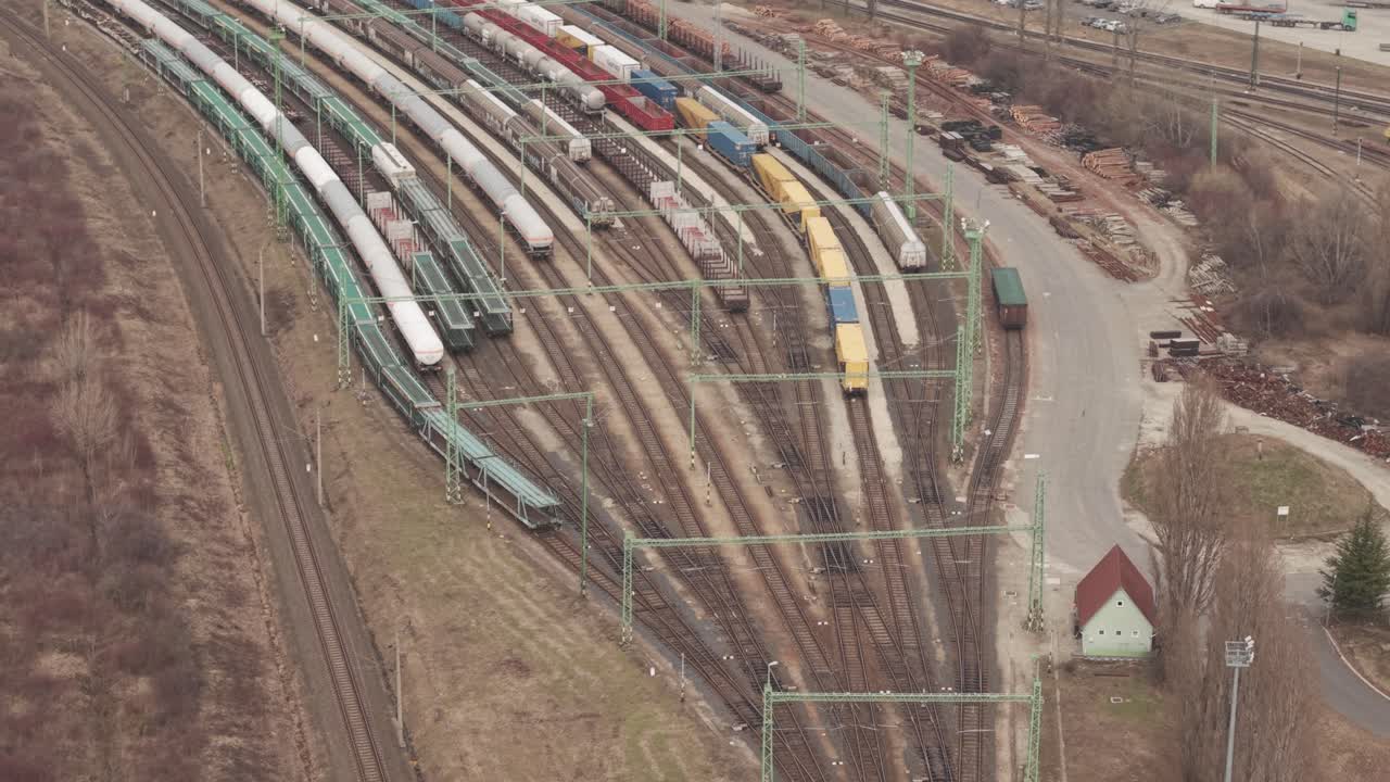 Luftaufnahme per Drohne von mehreren Güterzügen, die auf gekrümmten Eisenbahngleisen in einem großen Frachtterminal stehen. Bunte Schiffscontainer und Kesselwagen sind entlang der Gleise angeordnet