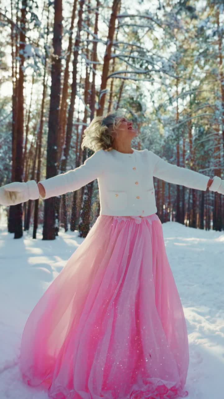 Donna gioiosa in abito rosa che si gode la neve che cade in una foresta invernale