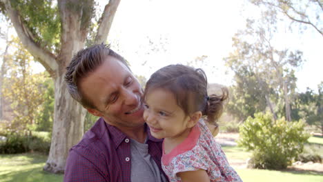 Dad-holding-toddler-daughter-in-his-arms-at-the-park