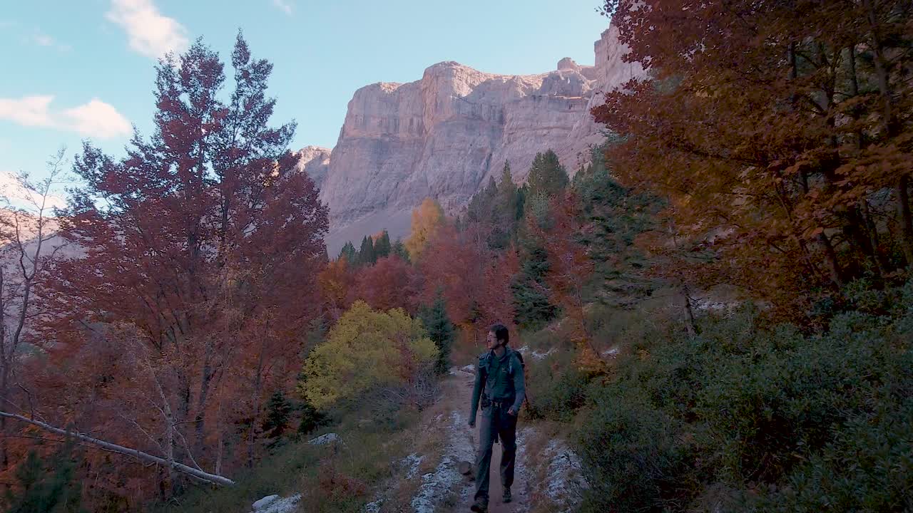 Front view of young Hiker man with trekking backpack walking on trail in dark autumn woods in Ordesa National Park, Spain
