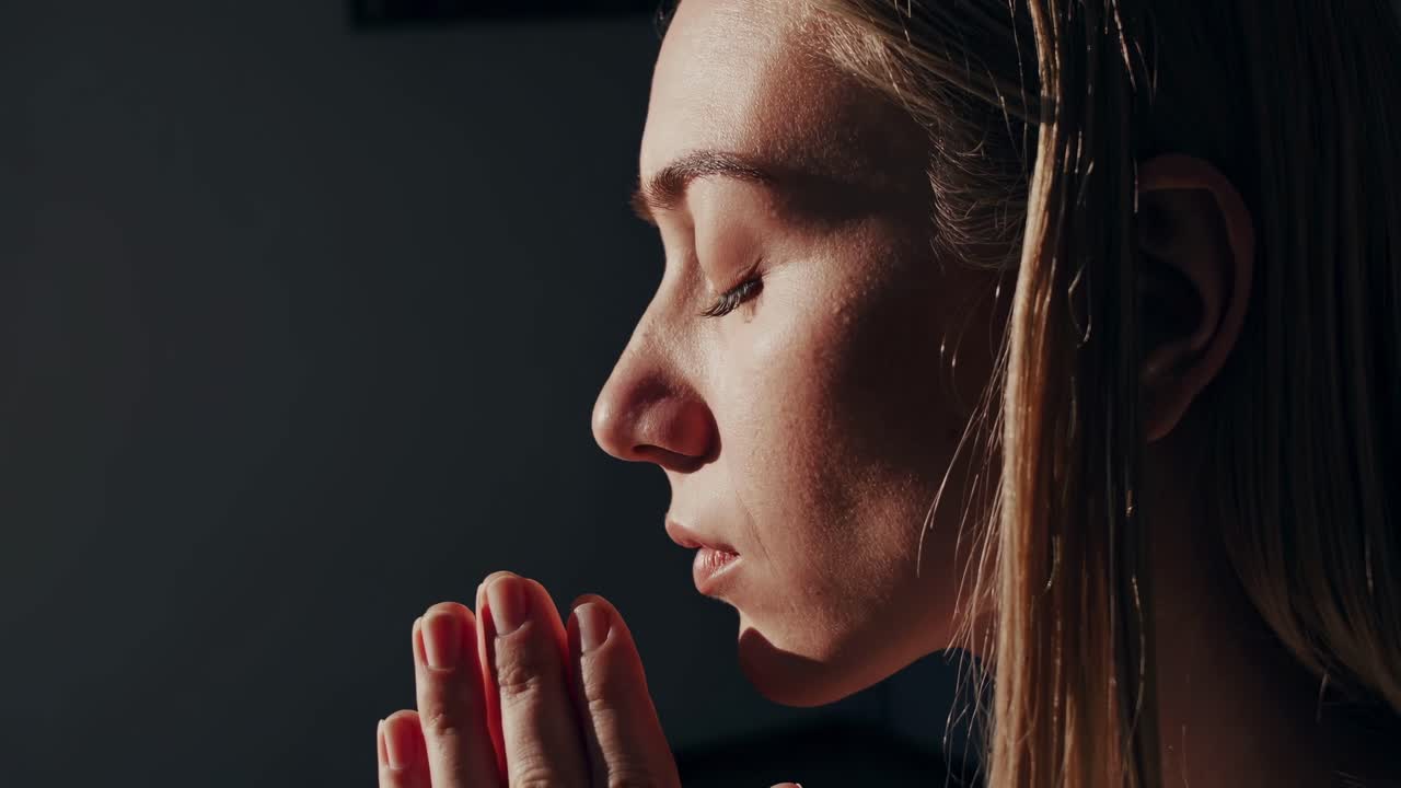 Close-up side profile of a woman meditating with hands in prayer, soft lighting, serene mood
