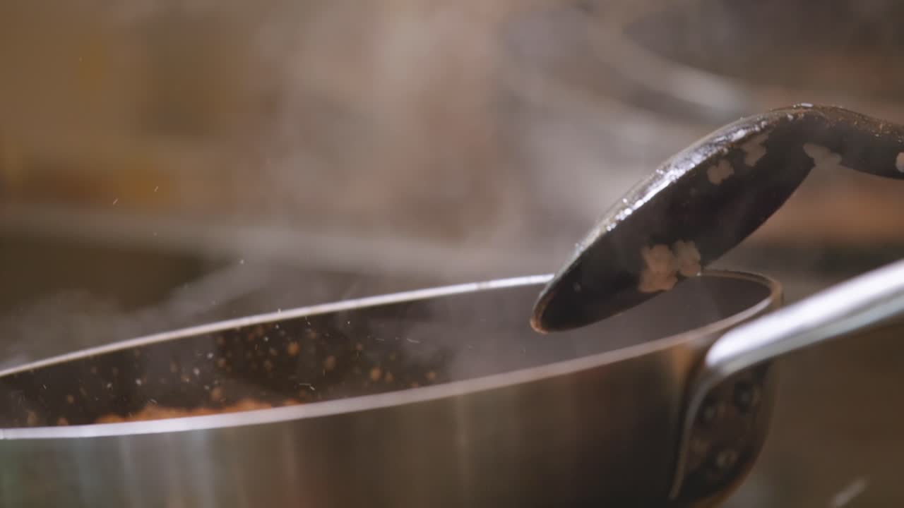 la mano de la hembra agita la sartén de risotto cocinando con el vapor de la espátula en primer plano