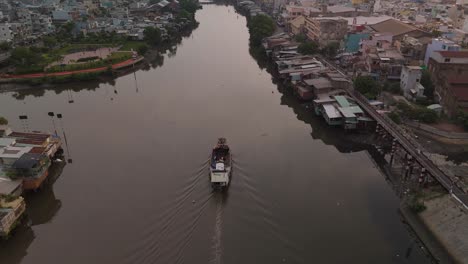 Vietnamese-river-boat-on-canal-with-urban-shacks-in-poor-neighborhood-of-Ho-Chi-Minh-City-showing-houses-and-skyline-in-beautiful-golden-evening-light