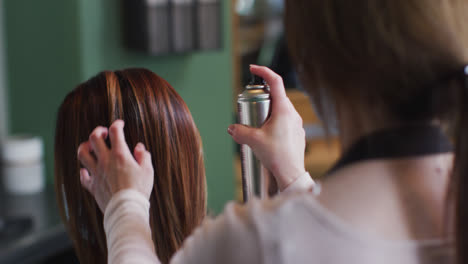 female hairdresser spraying hairspray on hair of female customer at hair salon