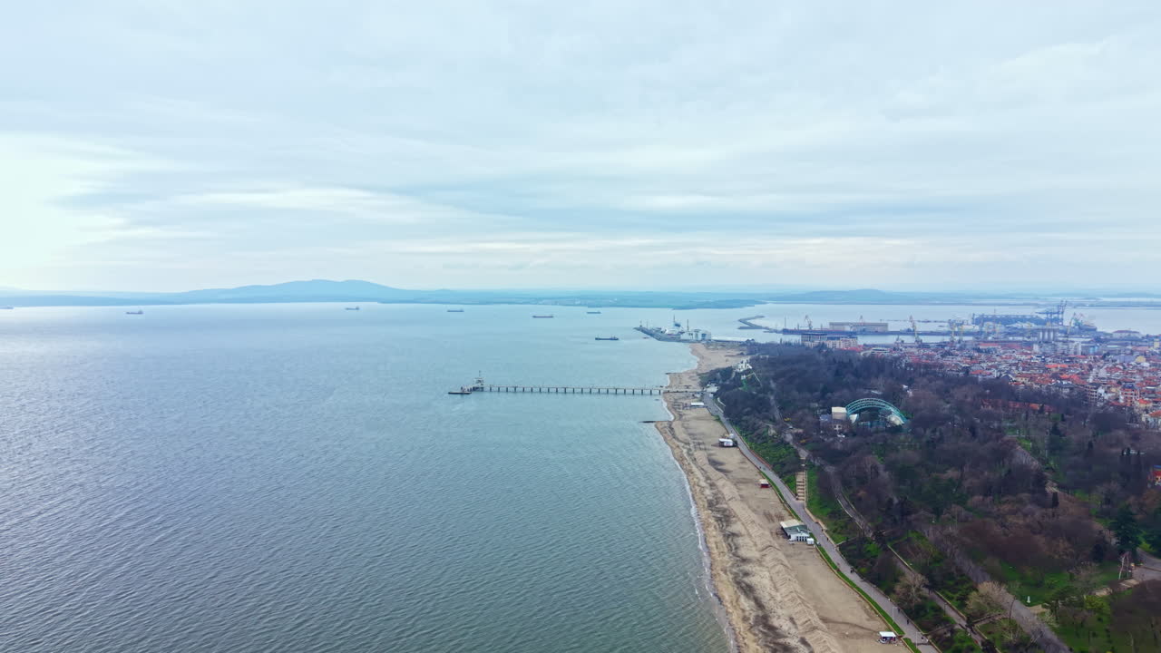 Vista de uma área costeira perto de uma cidade, com barcos e docas na água, durante um dia nublado, com a orla e a transição entre terra e mar.