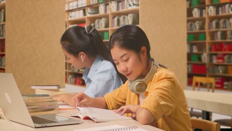 asian woman students with headphones reading books while sitting on the table with laptop in the library