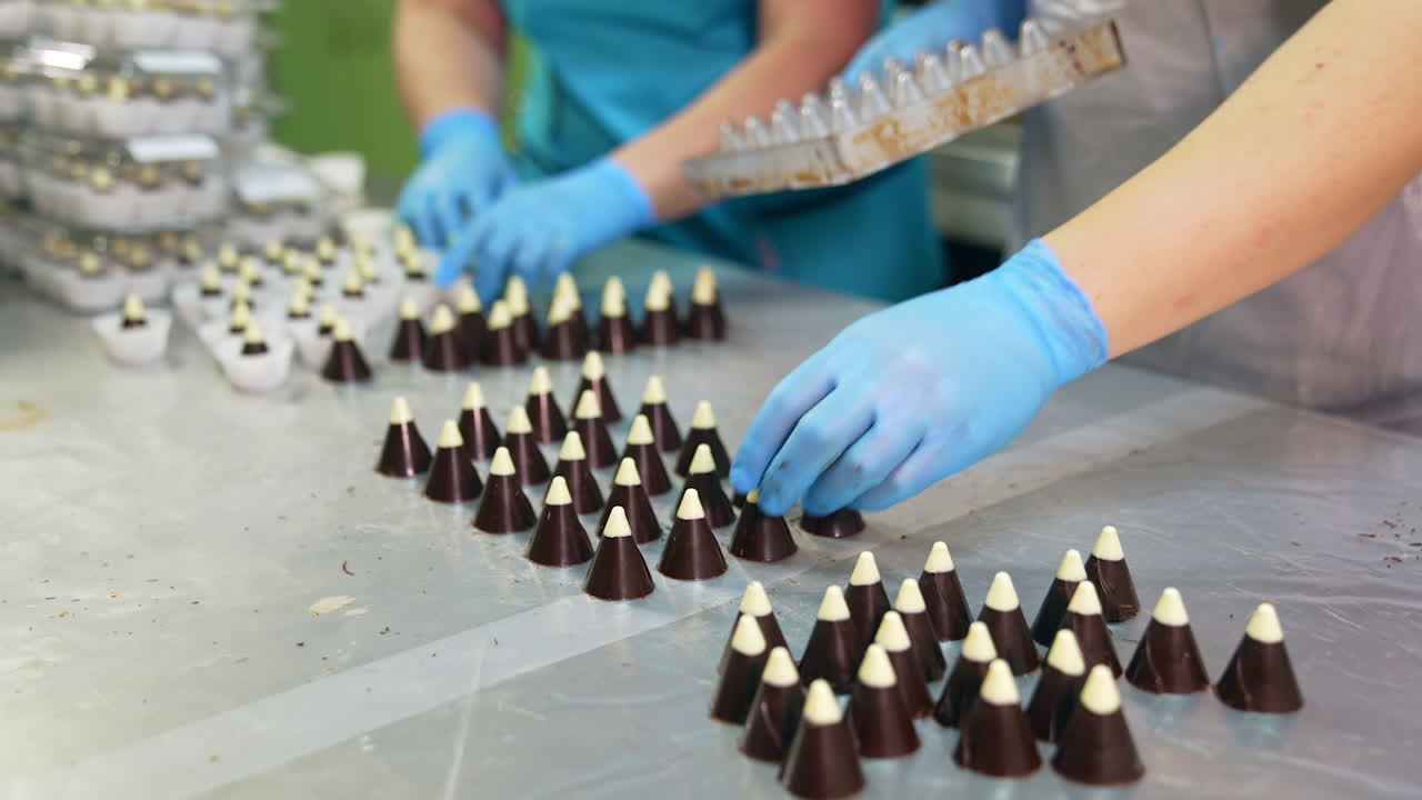 Little chocolate cones being extracted from the molds. Close up. Handmade chocolate candies packaging at the modern confectionery factory.