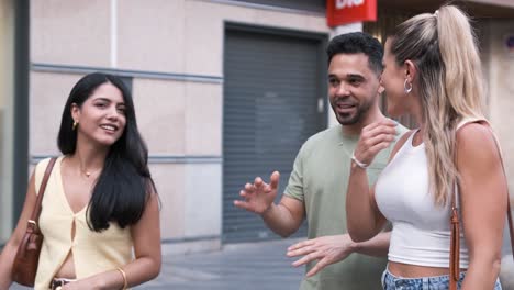 cheerful man talking to happy women while walking on city street