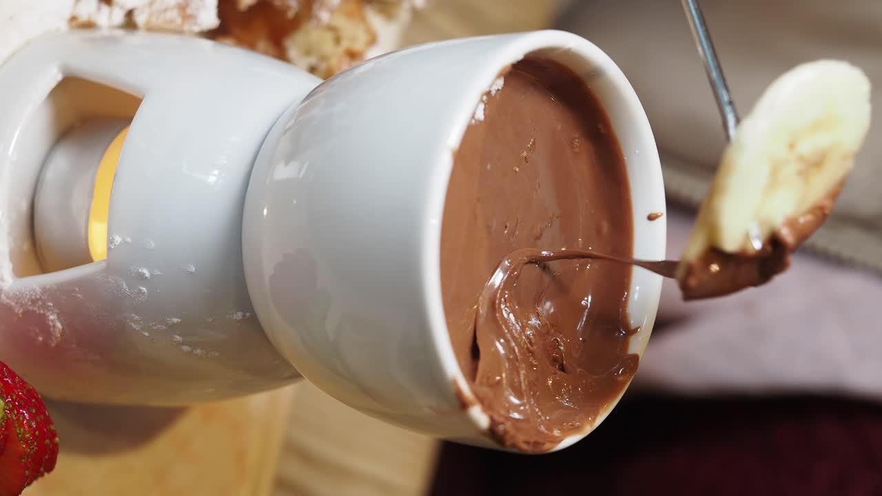 Dipping banana into warm chocolate fondue