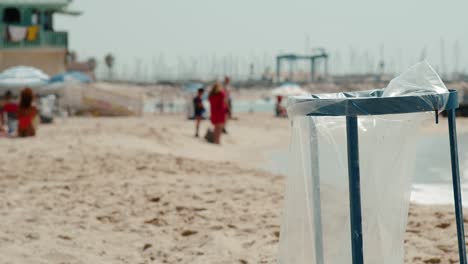 blue public trash can with plastic bag polluting at beach as blurry background people hang out