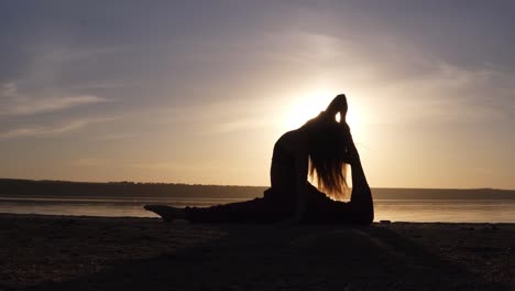 Young-pretty-woman-wearing-yoga-sportswear-working-out-against-sea,-doing-yoga-or-pilates-exercise.-Variation-of-monkey-god,-splits,-hanumanasana-with-backbend.-Full-length