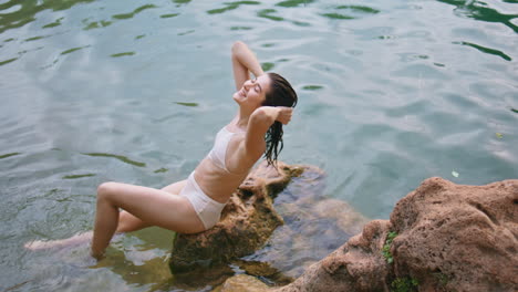 serene woman sitting rock wearing swimsuit. happy lady looking camera laughing