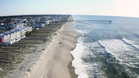 aerial drone flying over kure beach shoreline approaching pier