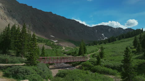 aerial cinematic drone early morning trailhead bridge over river grays and torreys 14er peaks rocky mountains colorado stunning landscape view mid summer green beautiful snow on top forward movement