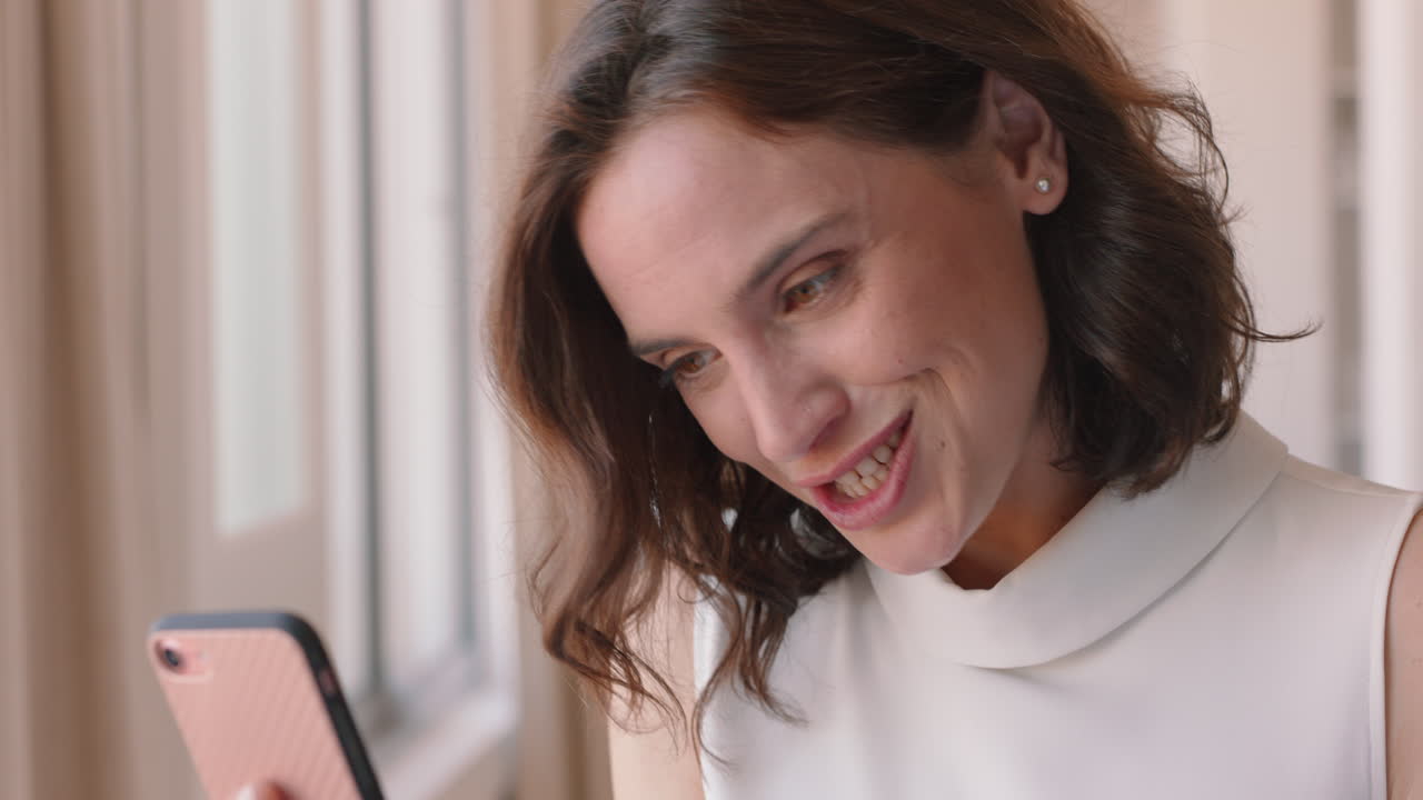 mujer hermosa teniendo video chat usando un teléfono inteligente sonriendo sorprendida disfrutando de buenas noticias charlando en teléfono móvil en casa