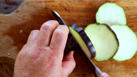 overhead view of male caucasian hands using knife to cut aubergine in disks