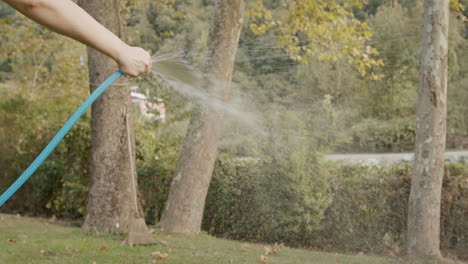 Hombre-Sosteniendo-La-Manguera-Azul-Y-Regando-El-Jardín-Empujando-Su-Dedo-Para-Rociar-Agua-En-Cámara-Lenta